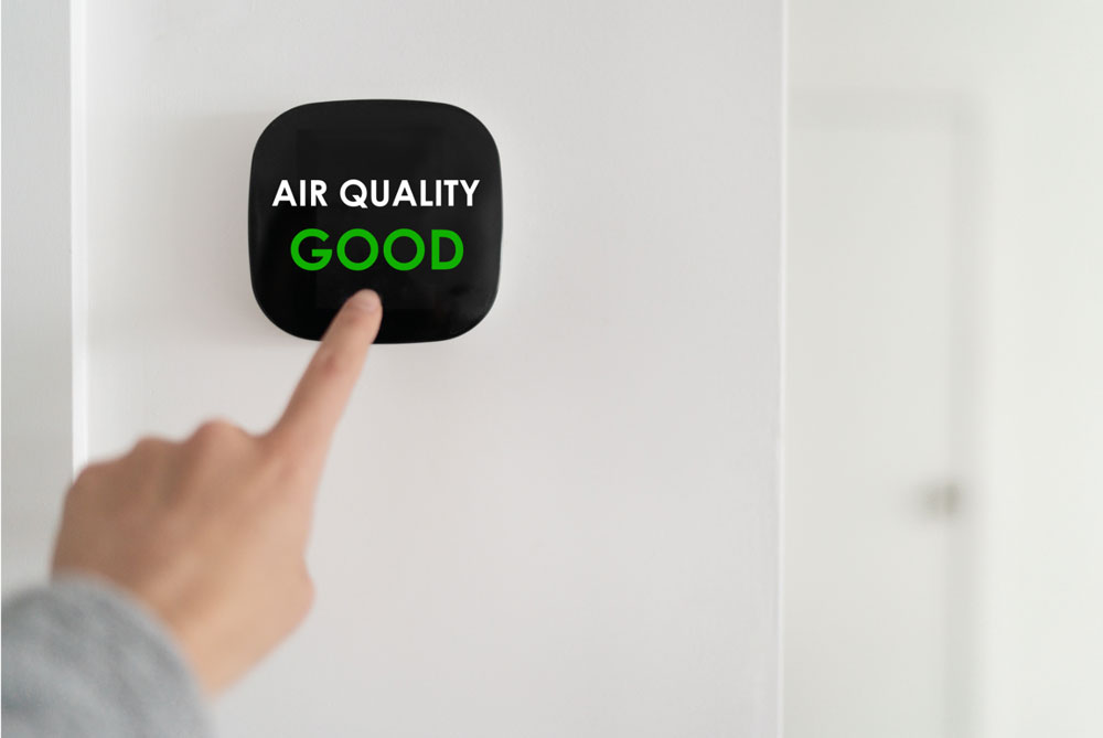 A person touching a modern air quality monitor displaying 'AIR QUALITY GOOD' on a wall.