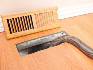 A flexible vacuum hose inserted into a floor vent for air duct cleaning