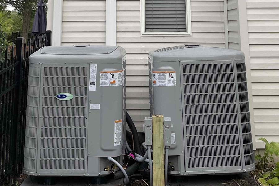 Two outdoor air conditioning units next to a home