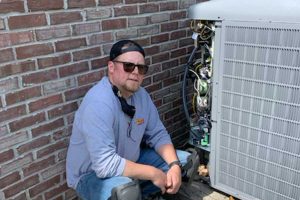HVAC technician kneeling next to an open outdoor air conditioning unit.