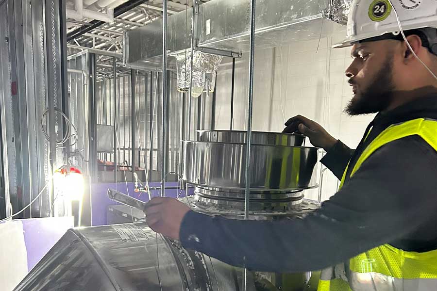 HVAC technician in a hard hat and safety vest working on ductwork